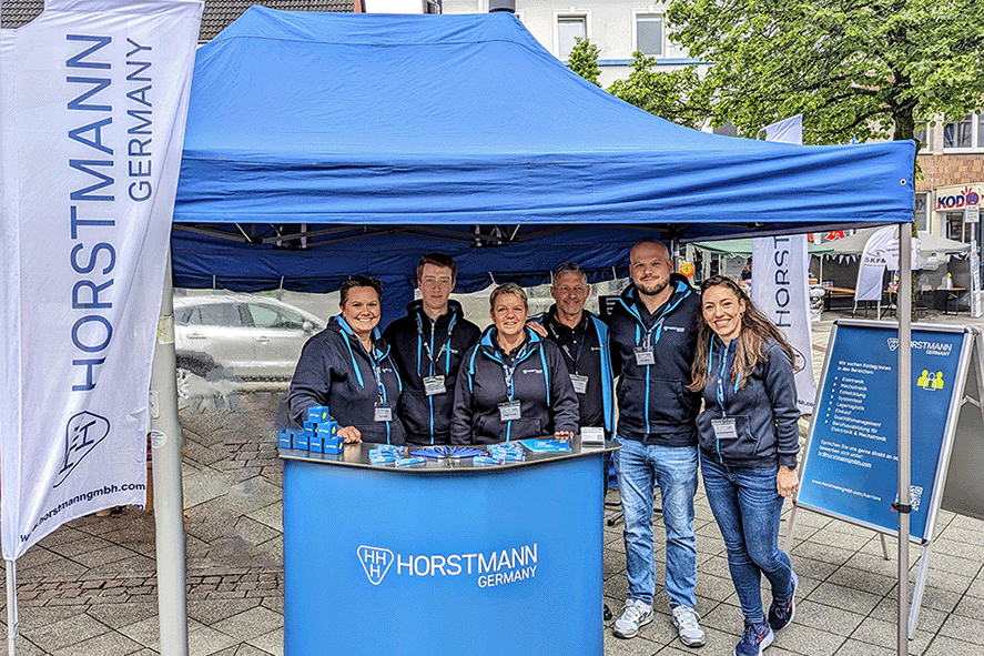 Gruppenfoto vom Stadtfest mit kleinem blauen Messestand und Horstmann Fahnen