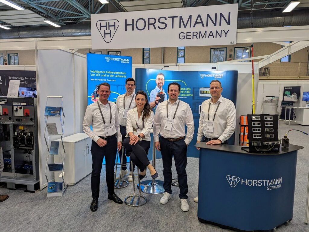 Gruppenfoto vom Horstmann-Team auf einem Messestand, auf dem aktuelle Produkte präsentiert werden. Alle lächeln freundlich in die Kamera