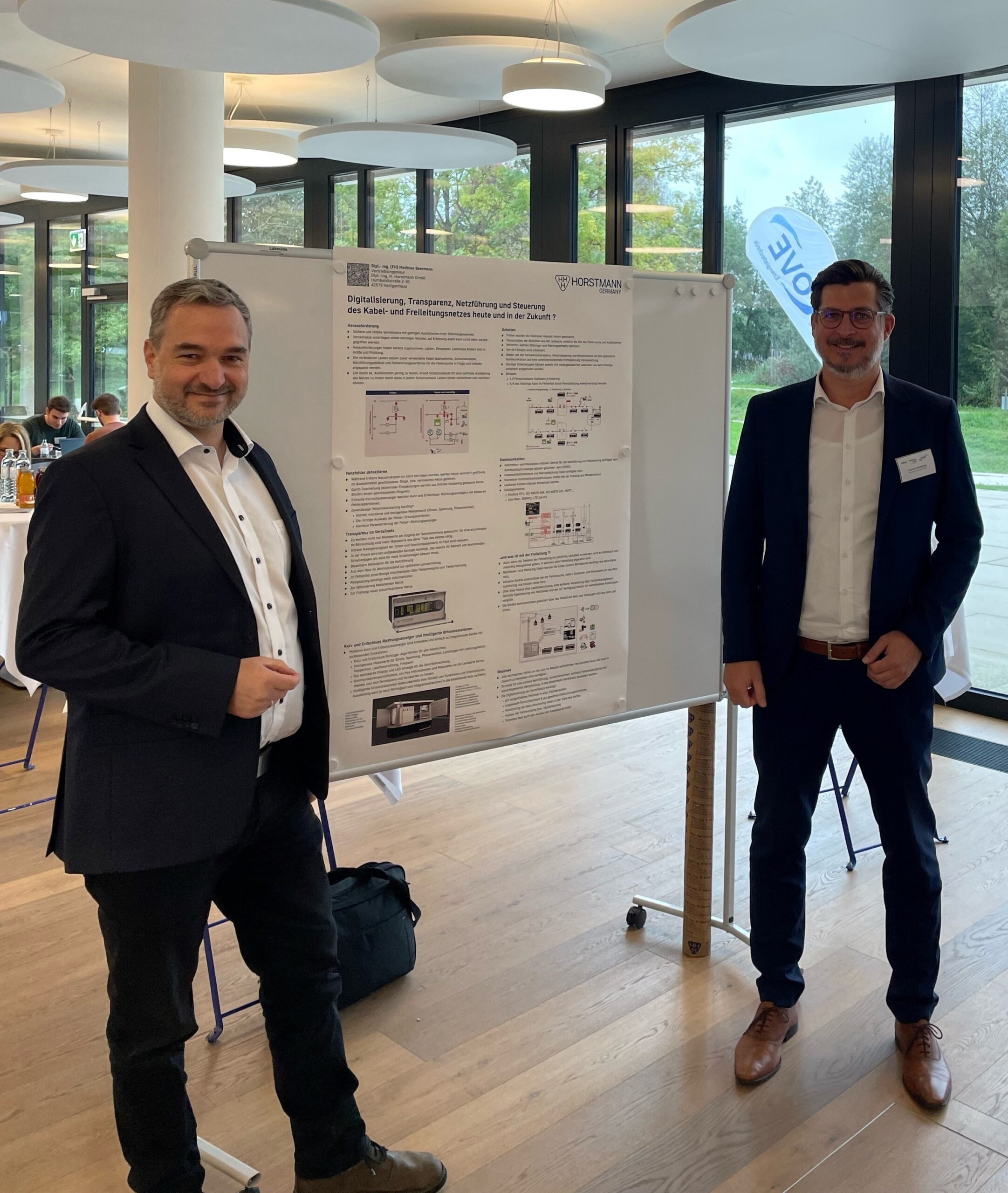 Firma Ertech und Horstmann präsentieren sich mit jeweils einen Mitarbeiter vor einer Vortragswand, auf der ein Horstmann Poster abgebildet ist