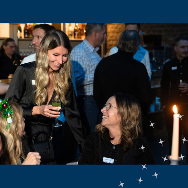Mitarbeiterin mit blonden, langen Haaren unterhält sich freudig mit einer anderen Teammitarbeiterin bei der Weihnachtsfeier
